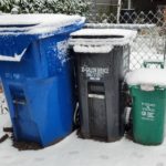 Recycling, garbage, and compost bins covered in snow.
