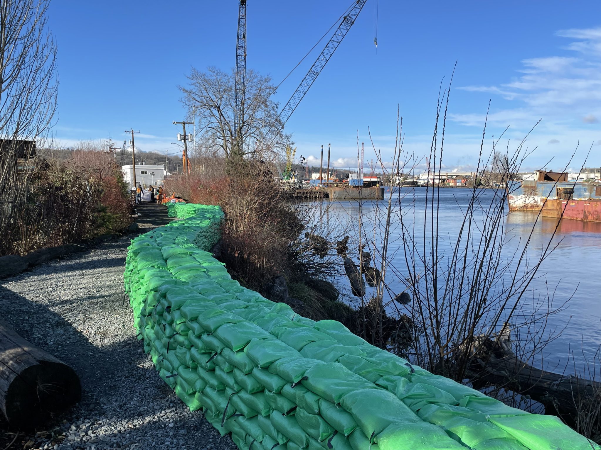 Photo shows a tall wall of sandbags along the river.