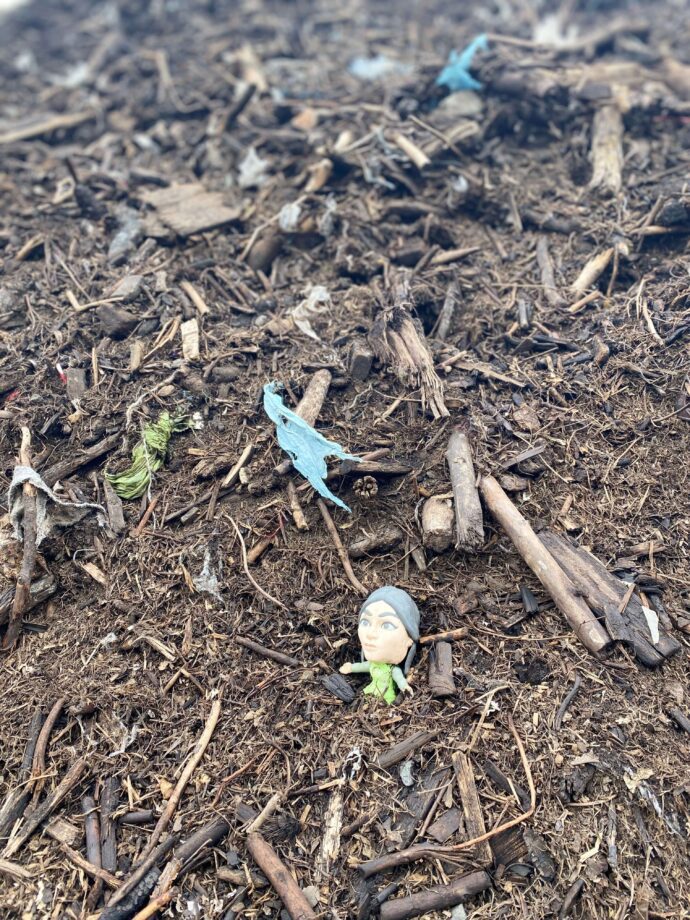 A close-up shot of processed compost that has plastic contamination. There are torn bits of green and blue plastic, along with an action figure.
