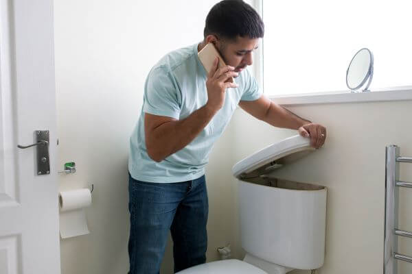 Man lifing toilet tank lid while calling aplumber.