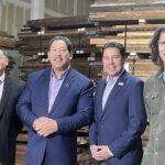 Four men pose in front of warehouse racks full of salvaged lumber.