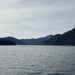 A lake surrounded by mountains and foothills beneath a sunny sky.