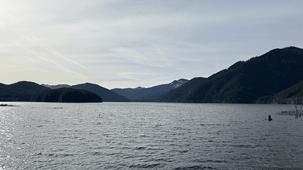 A lake surrounded by mountains and foothills beneath a sunny sky.
