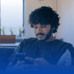 A male-presenting person sitting on a couch looking at their phone.